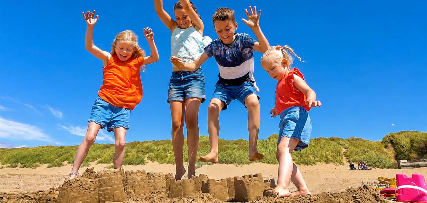 Children jumping over sandcastles on Brean Beach during a sunny family holiday in Somerset.